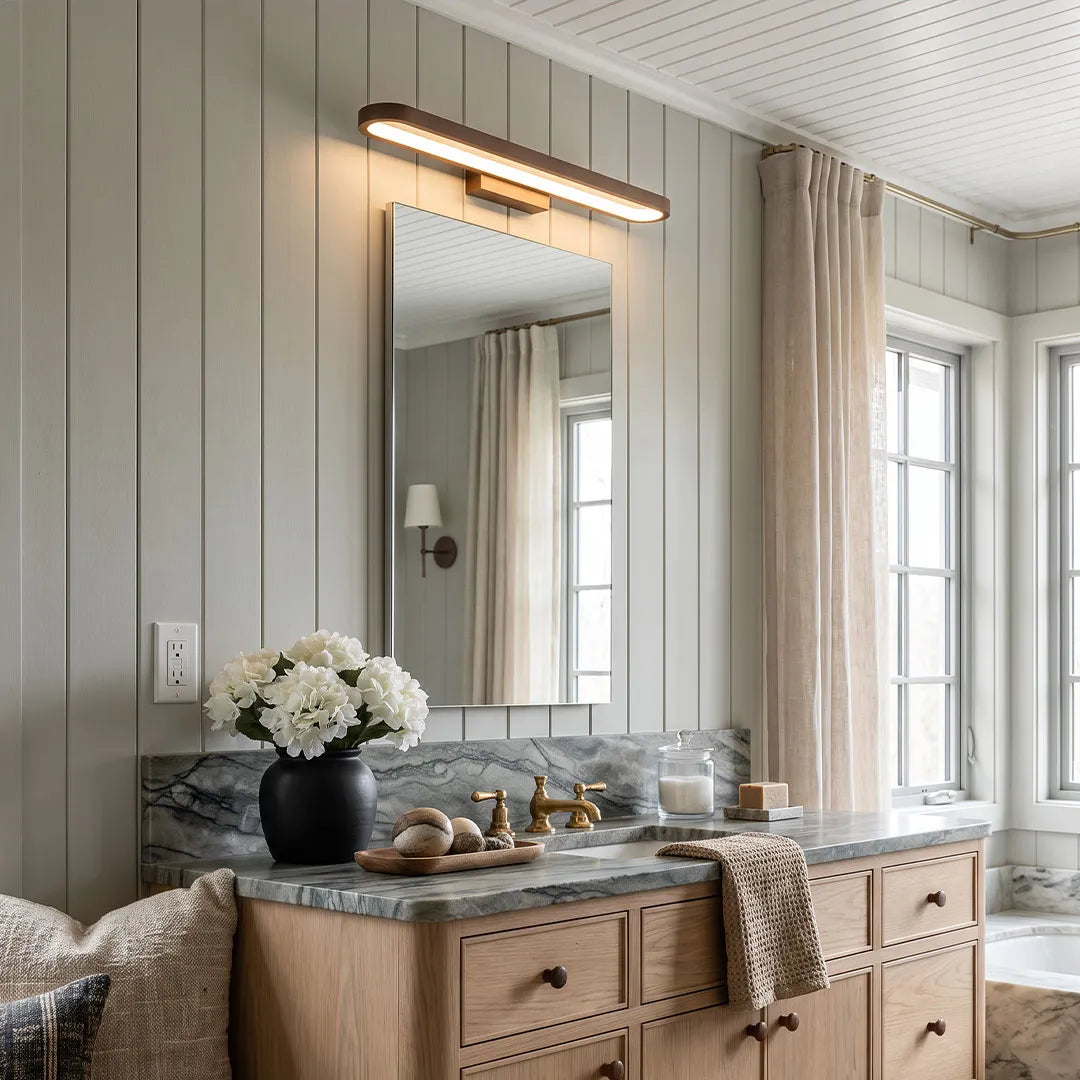 Bathroom vanity bar light mounted above a rectangular mirror in a bathroom with a wood vanity and marble countertop.