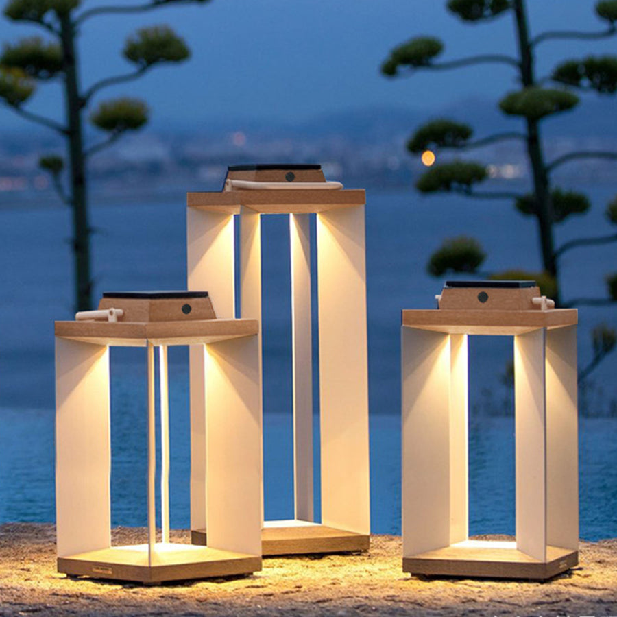 Three illuminated wooden lanterns creating ambient lighting on beach sand during twilight hour