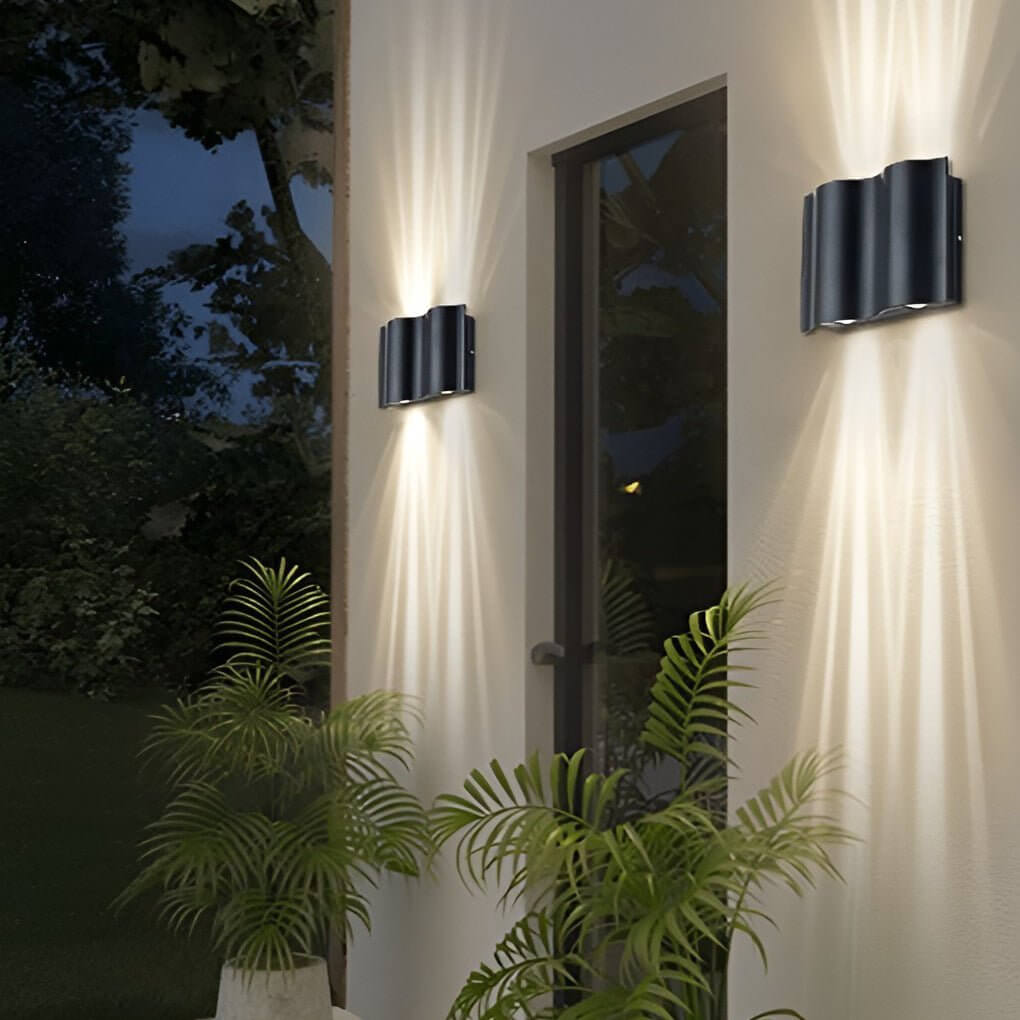 Beam wall light with a black finish, mounted near greenery, providing soft illumination.