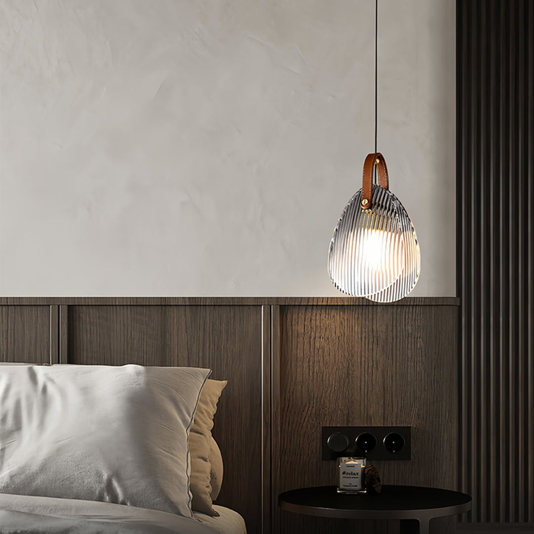 Hanging glass pendant light illuminating modern bedroom with wooden headboard and neutral decor
