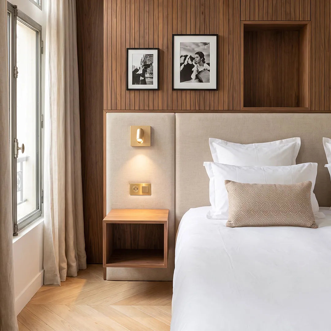 Wall mounted LED reading light installed above a bedside table in a bright modern bedroom.