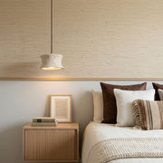 Drum pendant light fixture installed beside a bed with warm downward illumination and natural textures.