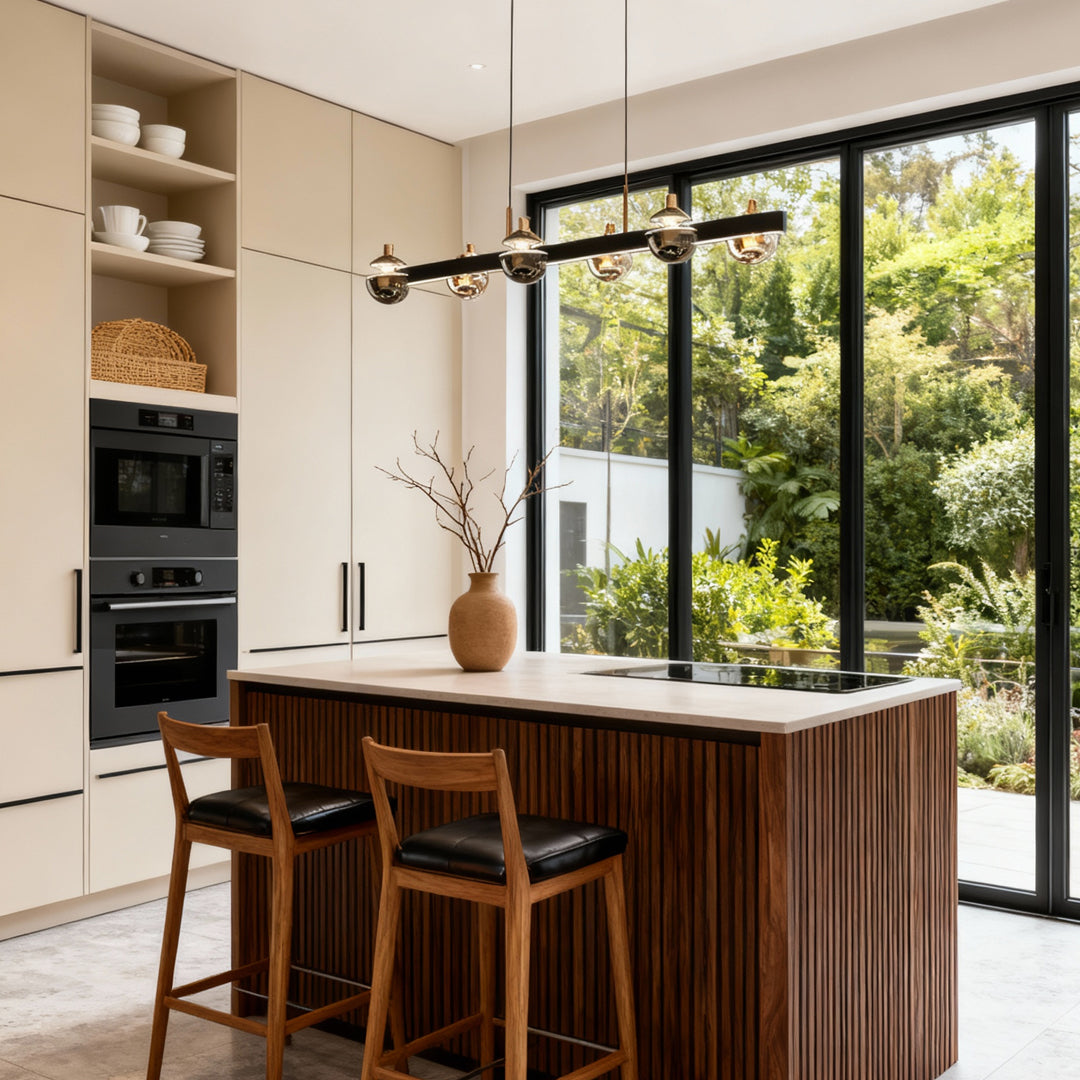 Black and gold modern chandelier highlighting kitchen space with dark island and large windows overlooking garden views