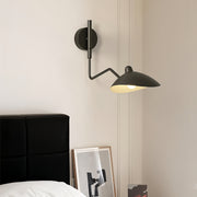Black articulated swing arm wall light with two adjustable heads, providing focused bedside reading light above a minimal headboard.