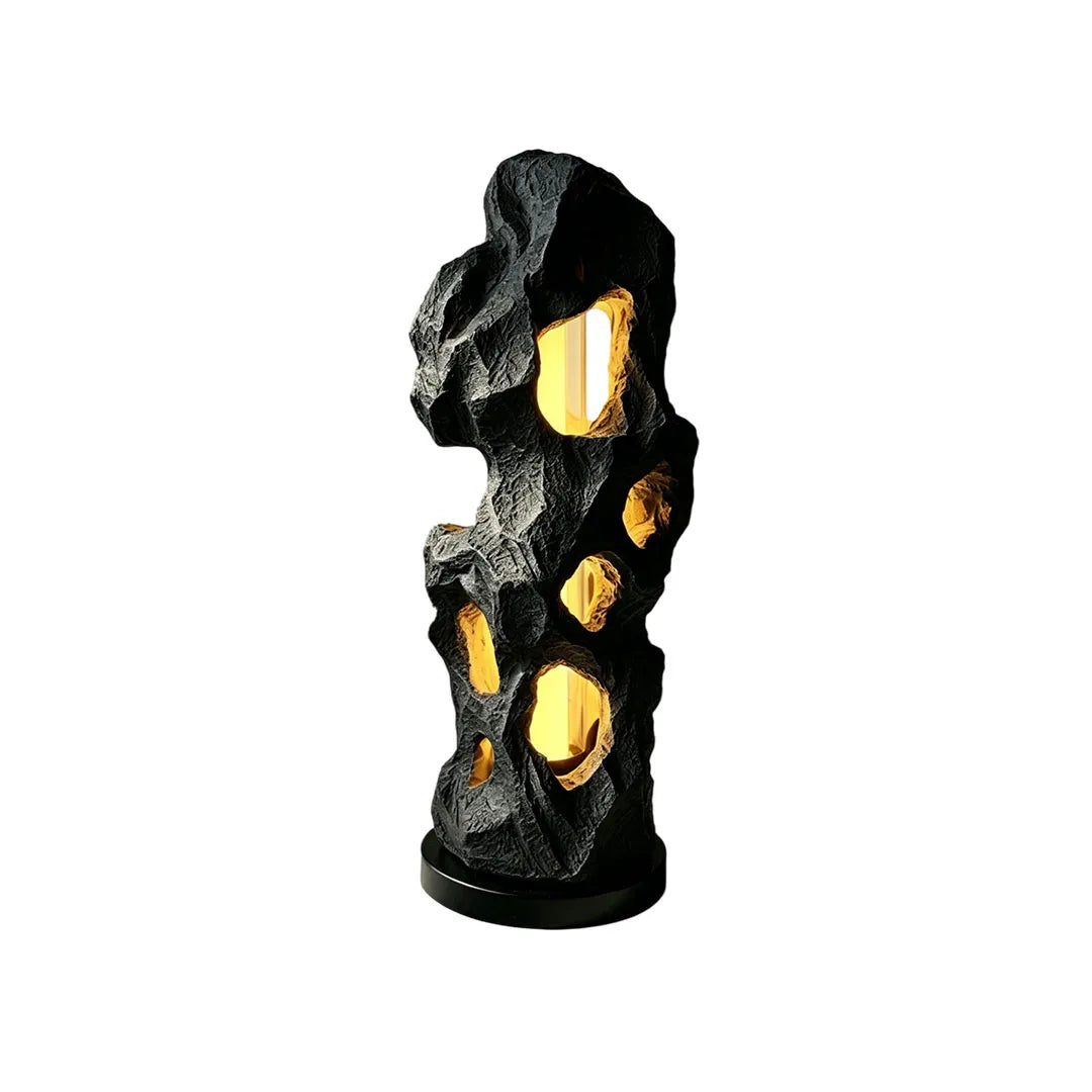 Black artistic table lamp with an abstract stone-inspired silhouette and glowing cutout details.