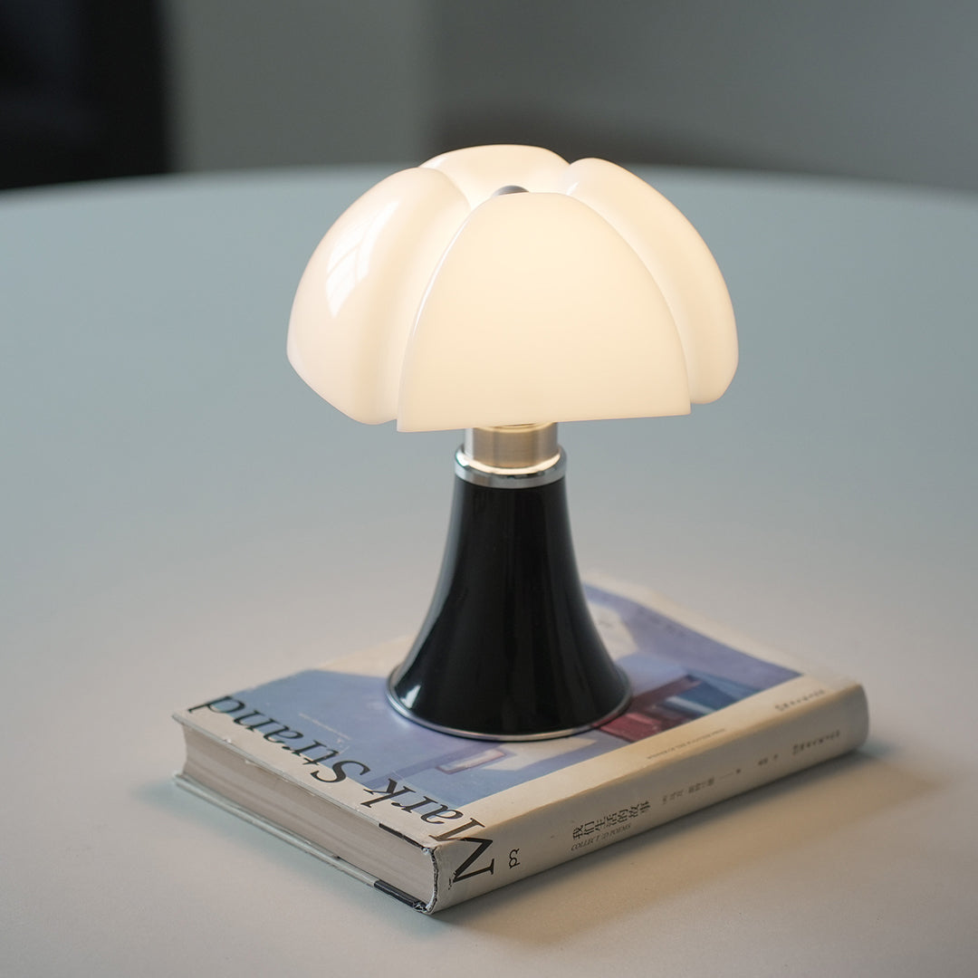 Black Bauhaus mushroom lamp on a book, creating cozy bedside lighting.
