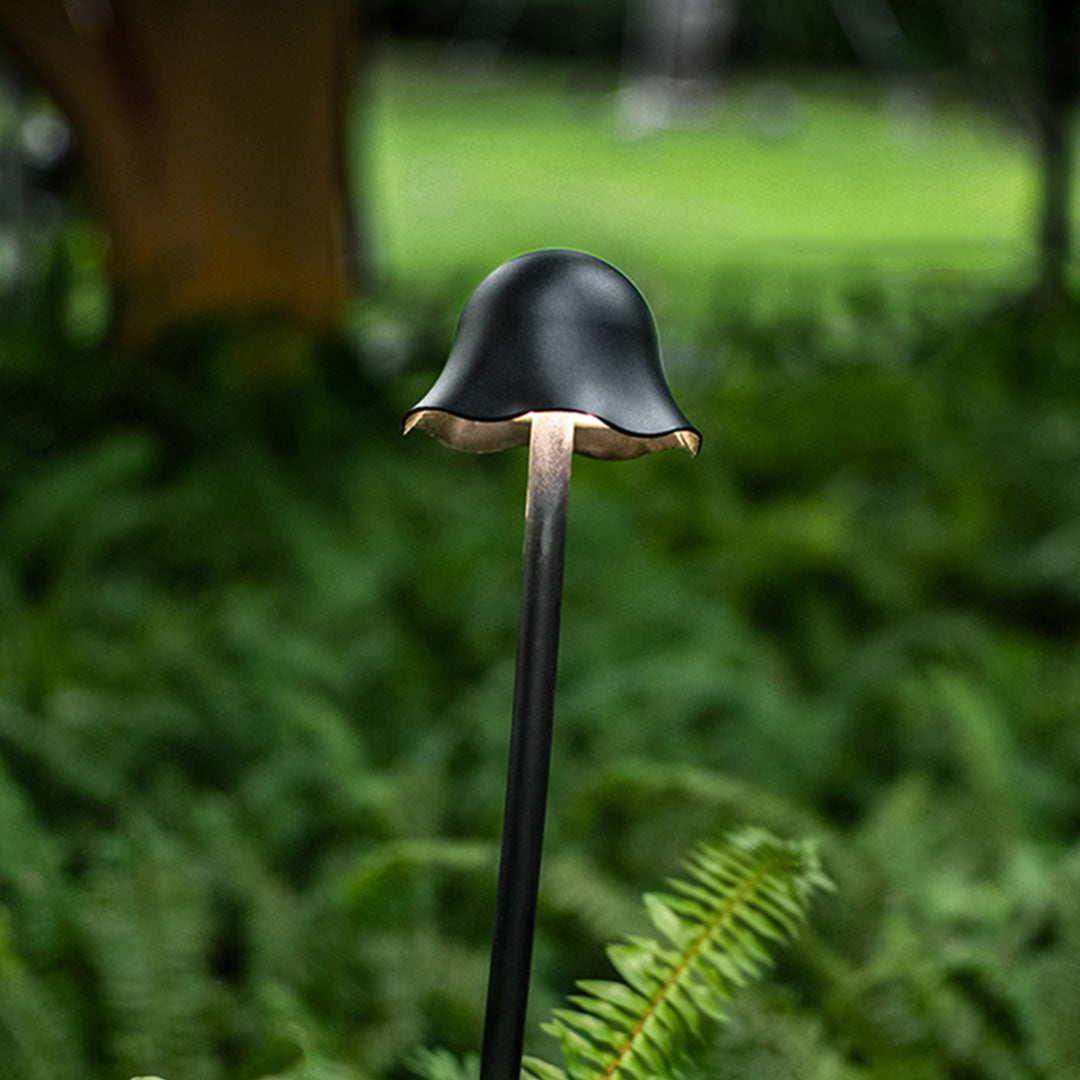 Single black outdoor landscape light with bell shade illuminating natural woodland setting with green vegetation