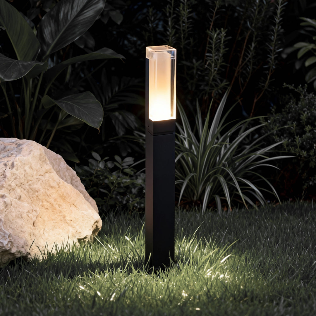 Black bollard light highlighting garden rocks and greenery at night