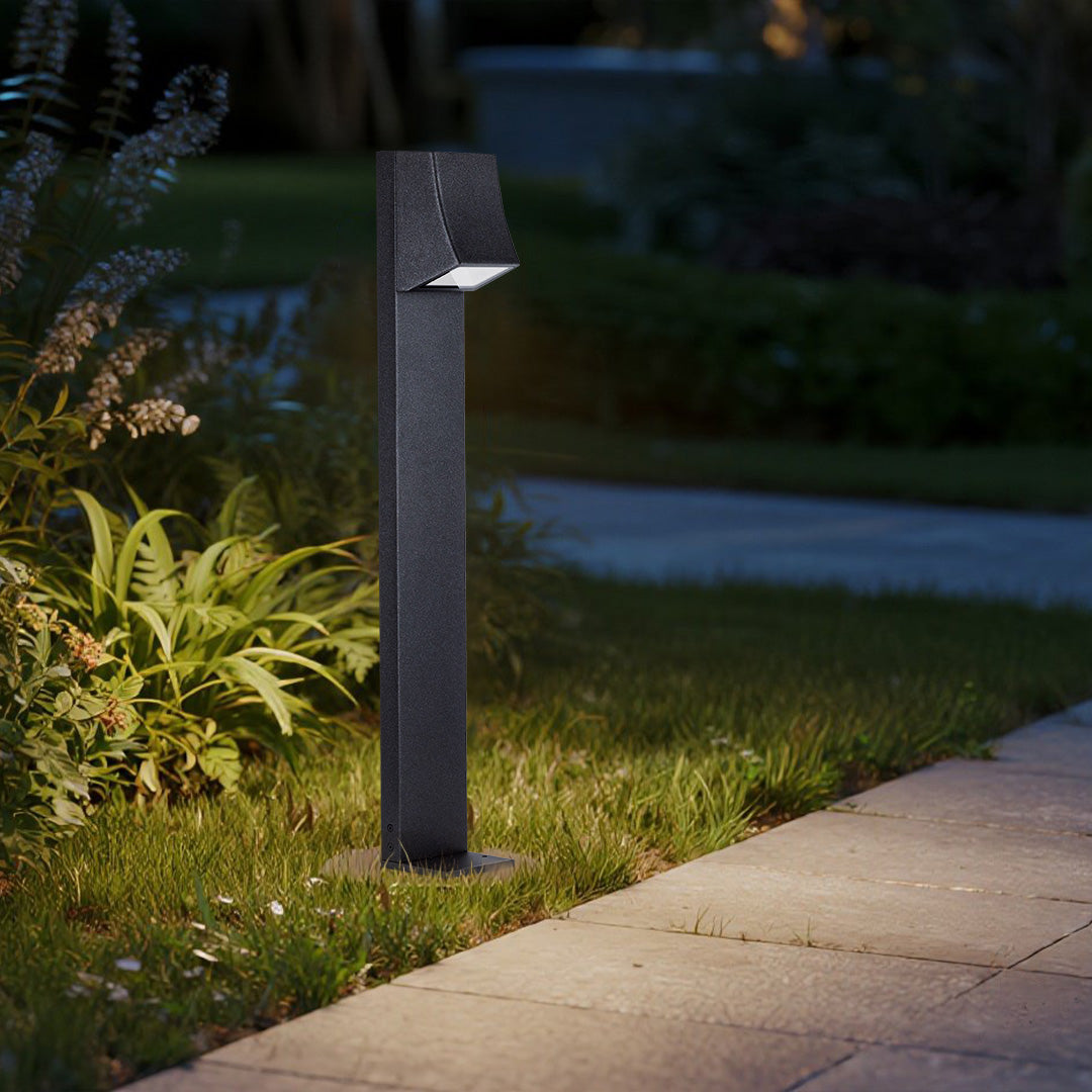 Black outdoor bollard light installed next to grass and flowerbed