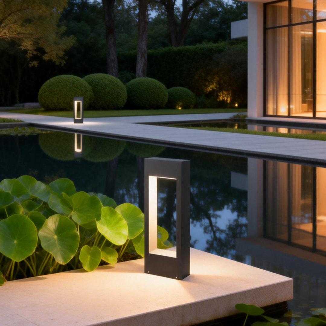 Modern black bollard light placed beside a pool reflecting warm landscape lighting.
