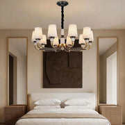 Black brass chandelier installed above a bedroom with elegant white shades and warm ambient lighting.