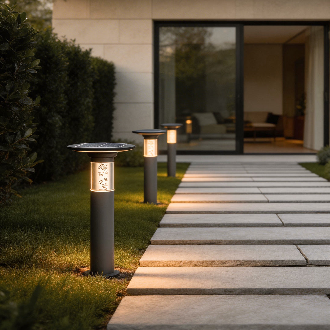 Black brass path lights illuminating a modern garden walkway with warm directional glow.