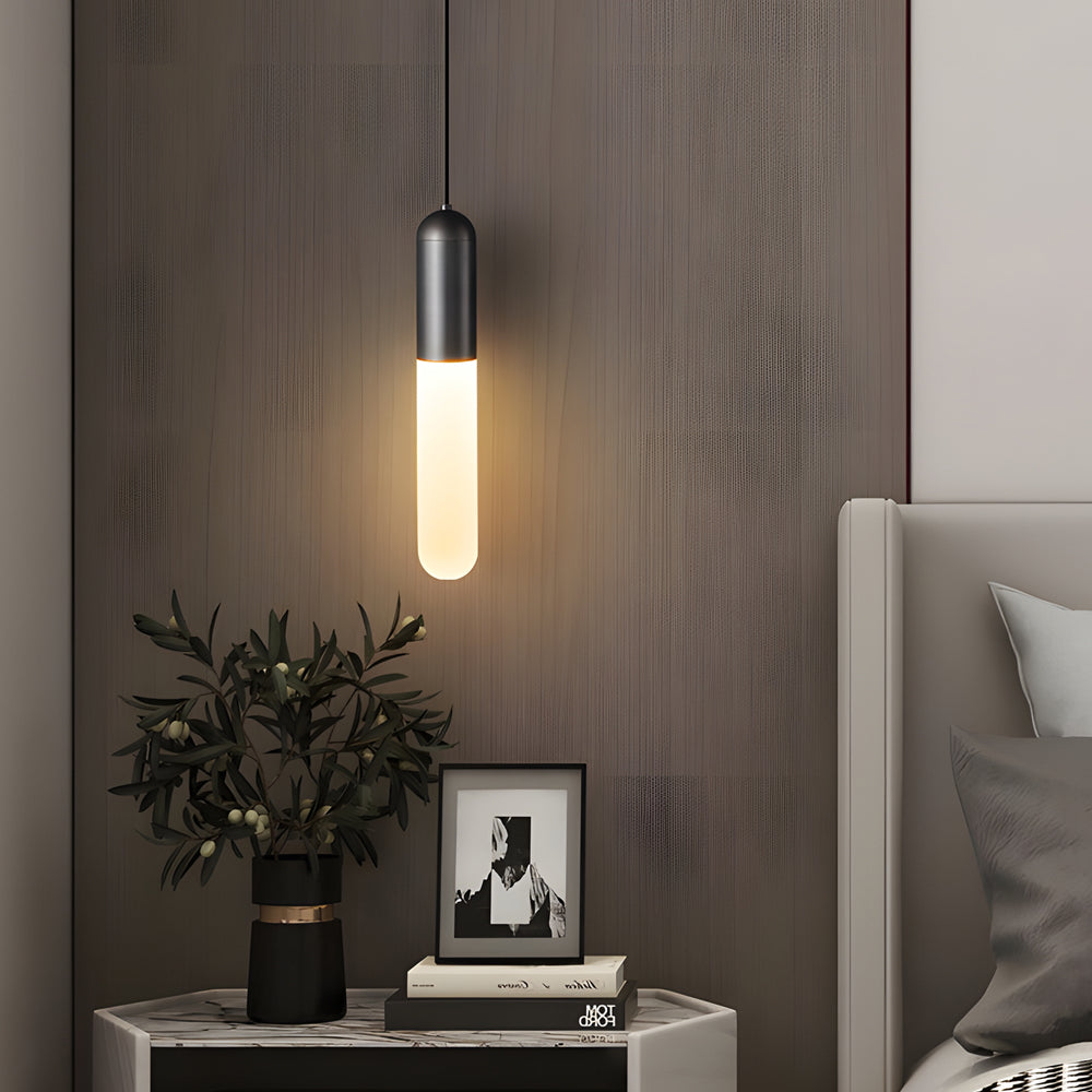 Modern black Gold Capsule Pendant Light variant hanging over a bedside table with a green plant.