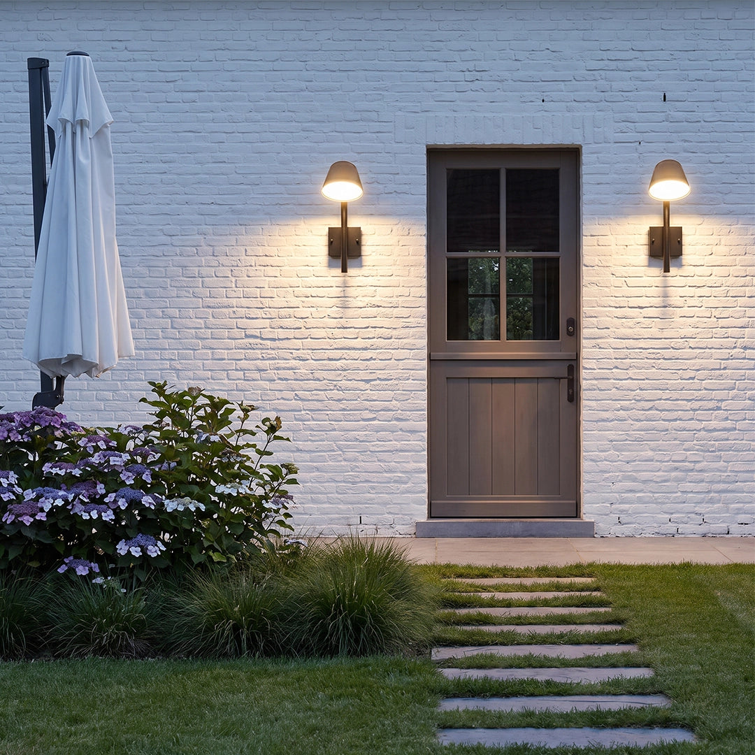 Black cone wall sconce pair flanking a back door and casting warm light across a white brick exterior.