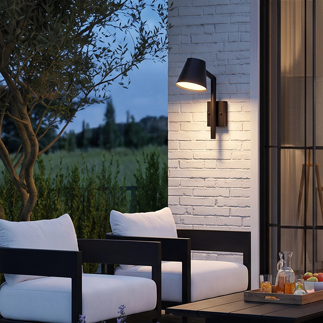 Black cone wall sconce casting warm downward illumination beside a modern outdoor seating area.