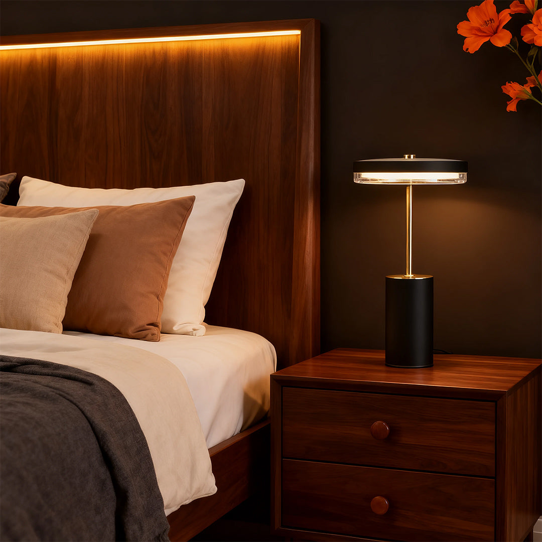 Black cylinder table lamps with a sleek, gold stem and ring light on a dark wooden nightstand.