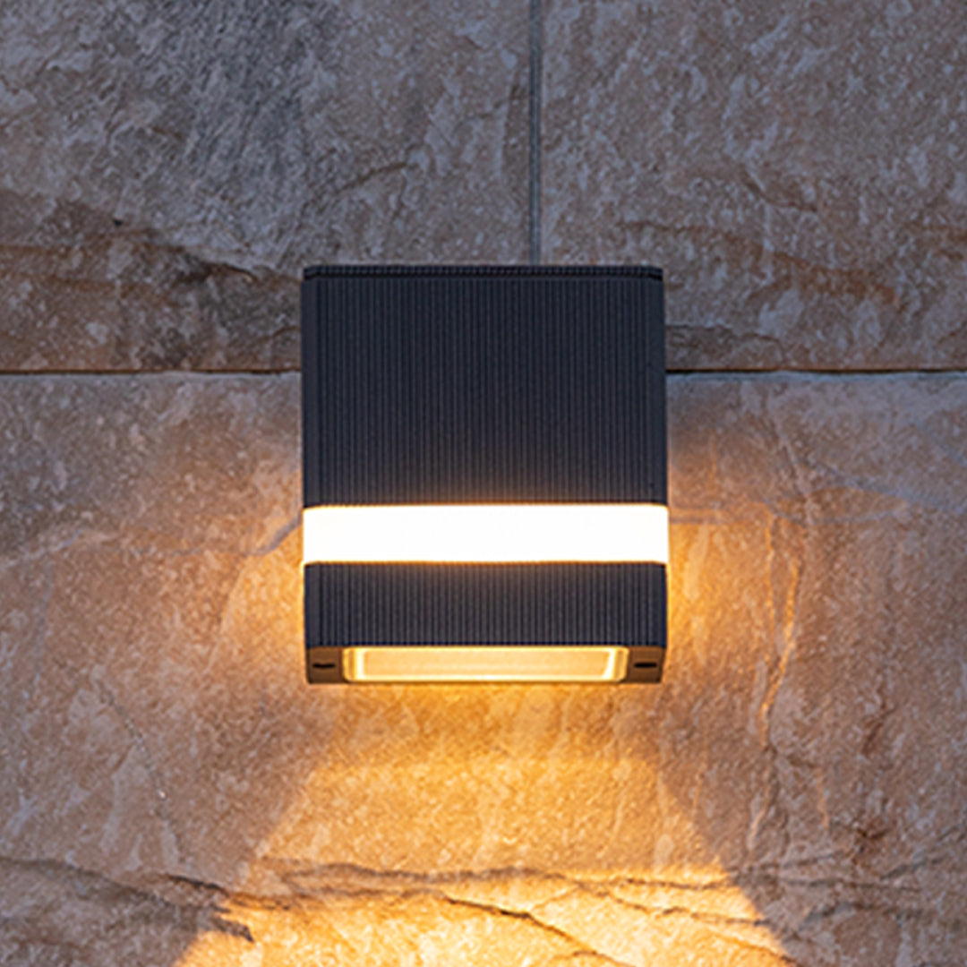 Black cylindrical garden wall light with horizontal stripe creating warm glow on stone tile