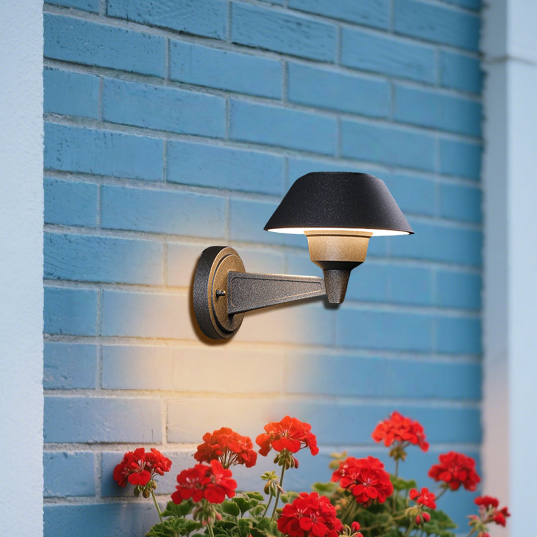 Contemporary outdoor wall sconce with conical shade casting warm light on white siding