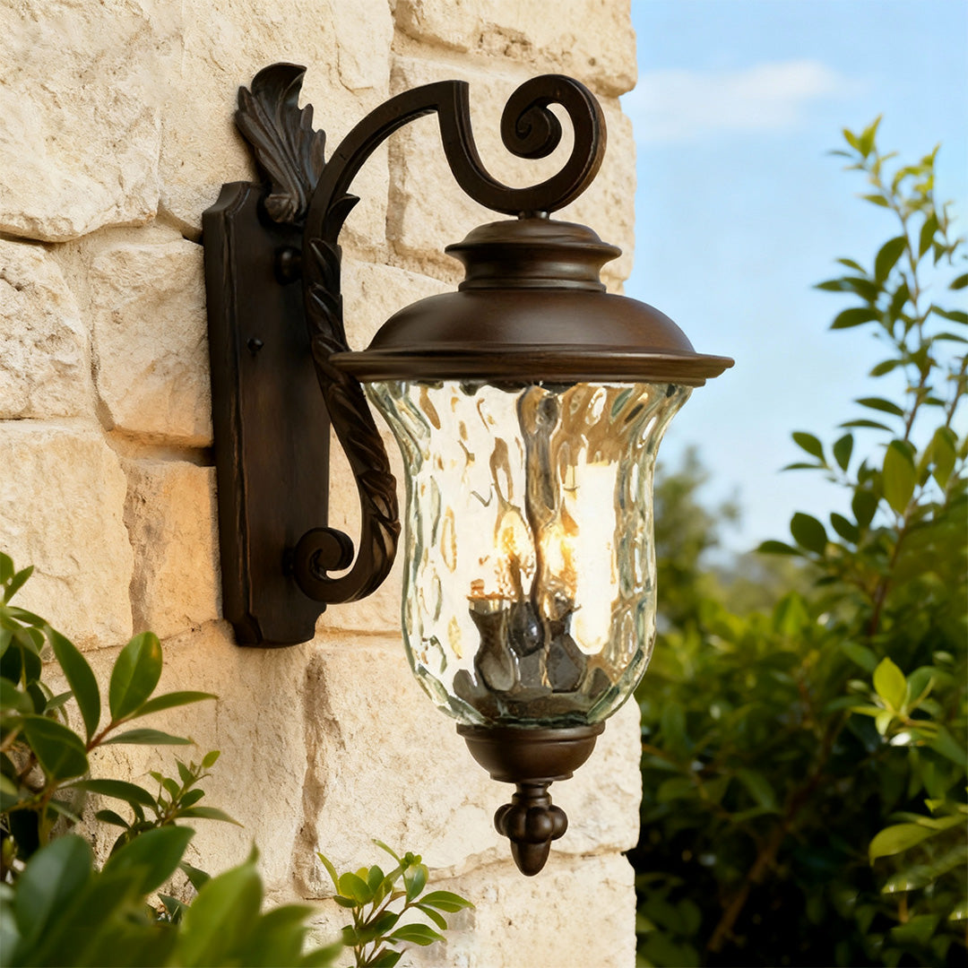 Black exterior wall light providing ambient lighting on stone facade with foliage and blue sky