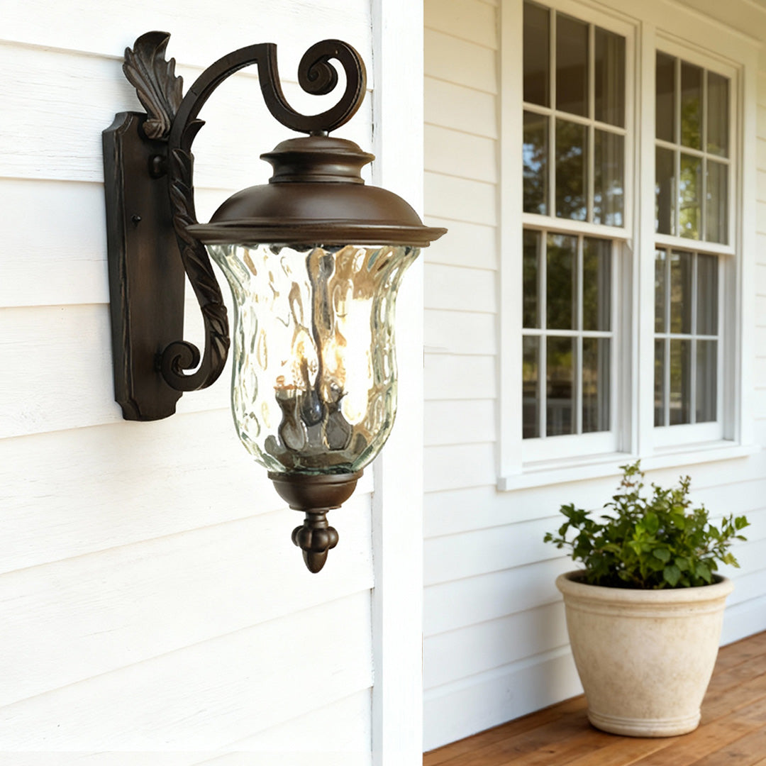 Black exterior wall light mounted on white siding near window with potted plant and greenery