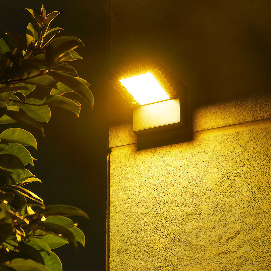 Black finish wall mount outdoor light fixtures illuminating a stucco wall and nearby foliage with warm light.