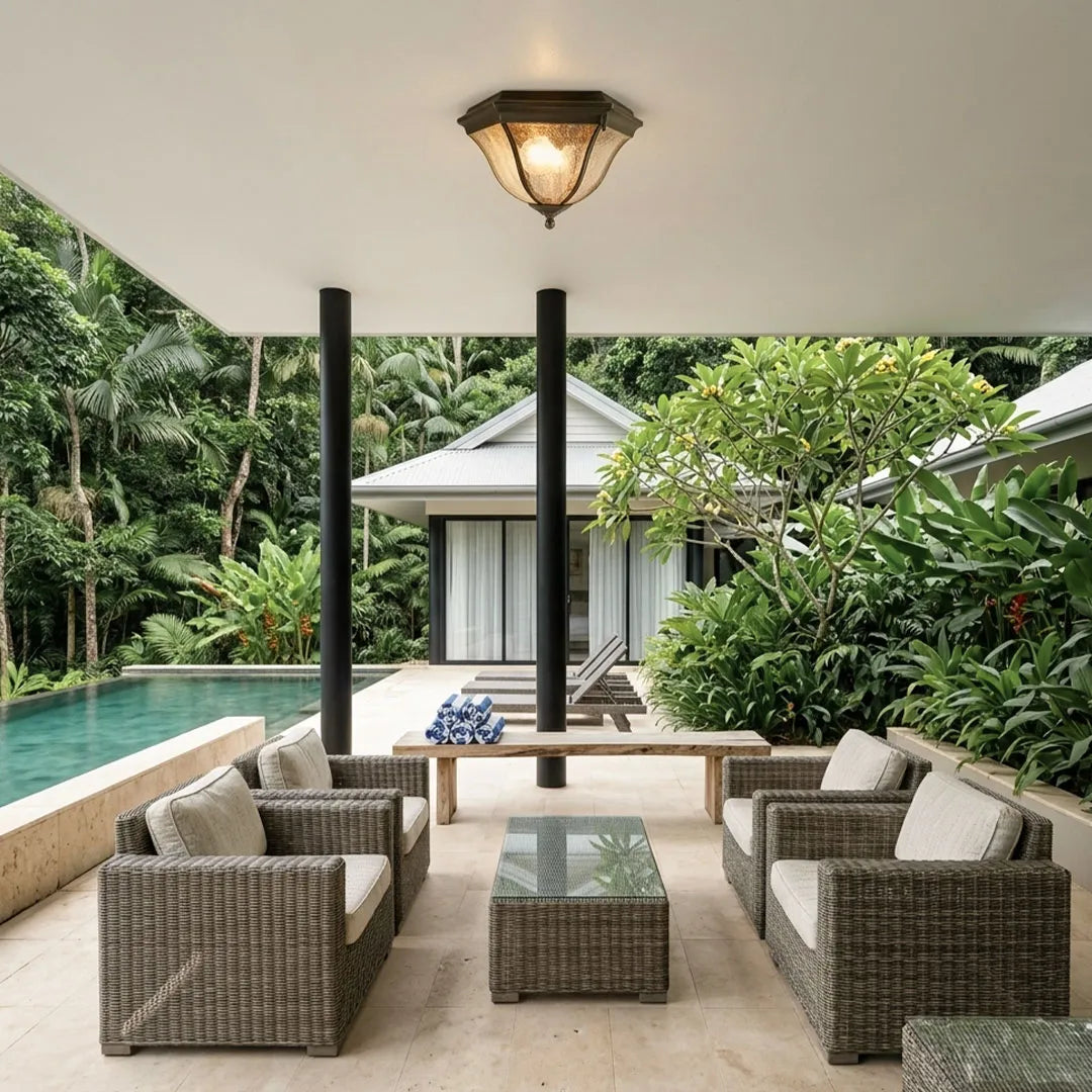 Black flush mount light fixture illuminating a covered poolside patio with woven outdoor seating.