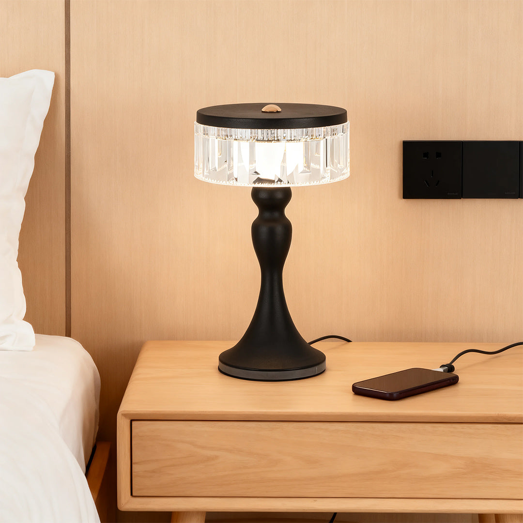 Black base forged iron table lamps style with a crystal shade charging next to a bed on a light wood nightstand.