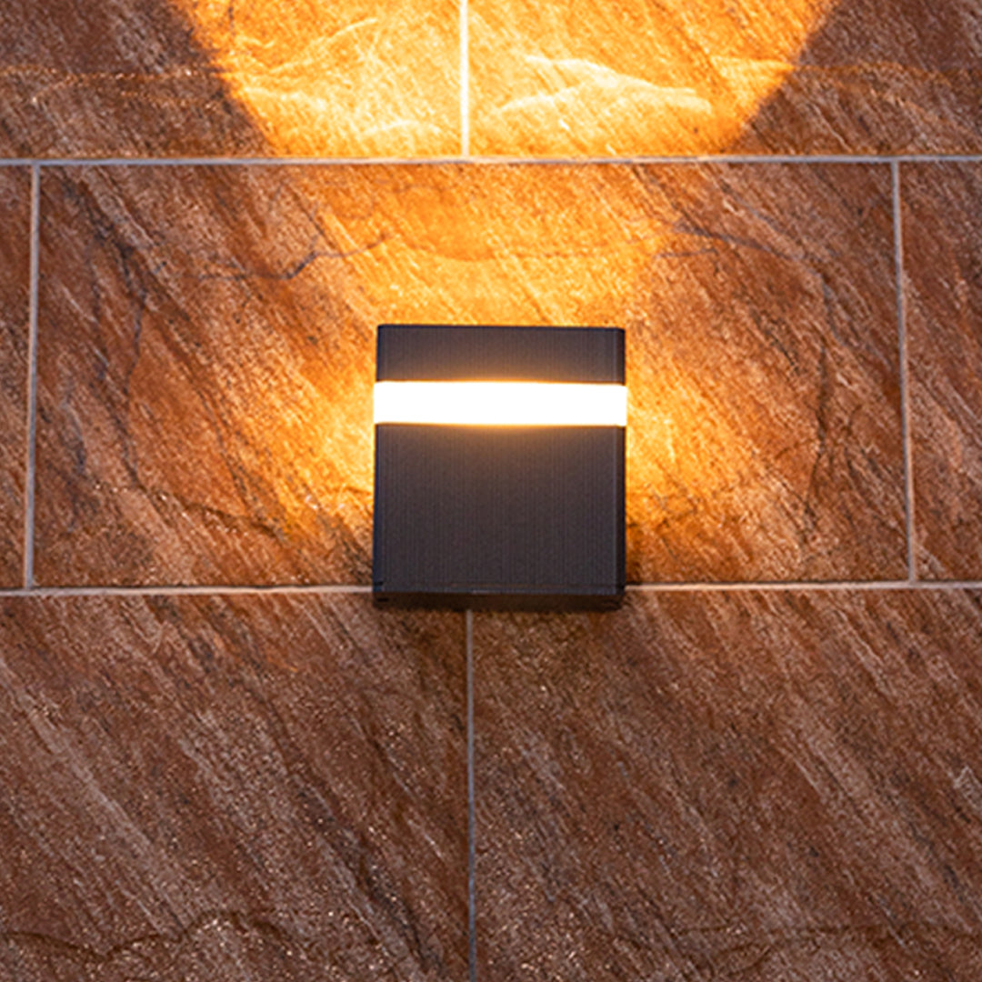 Black garden wall light creating dramatic uplighting and downlighting on textured wood surface