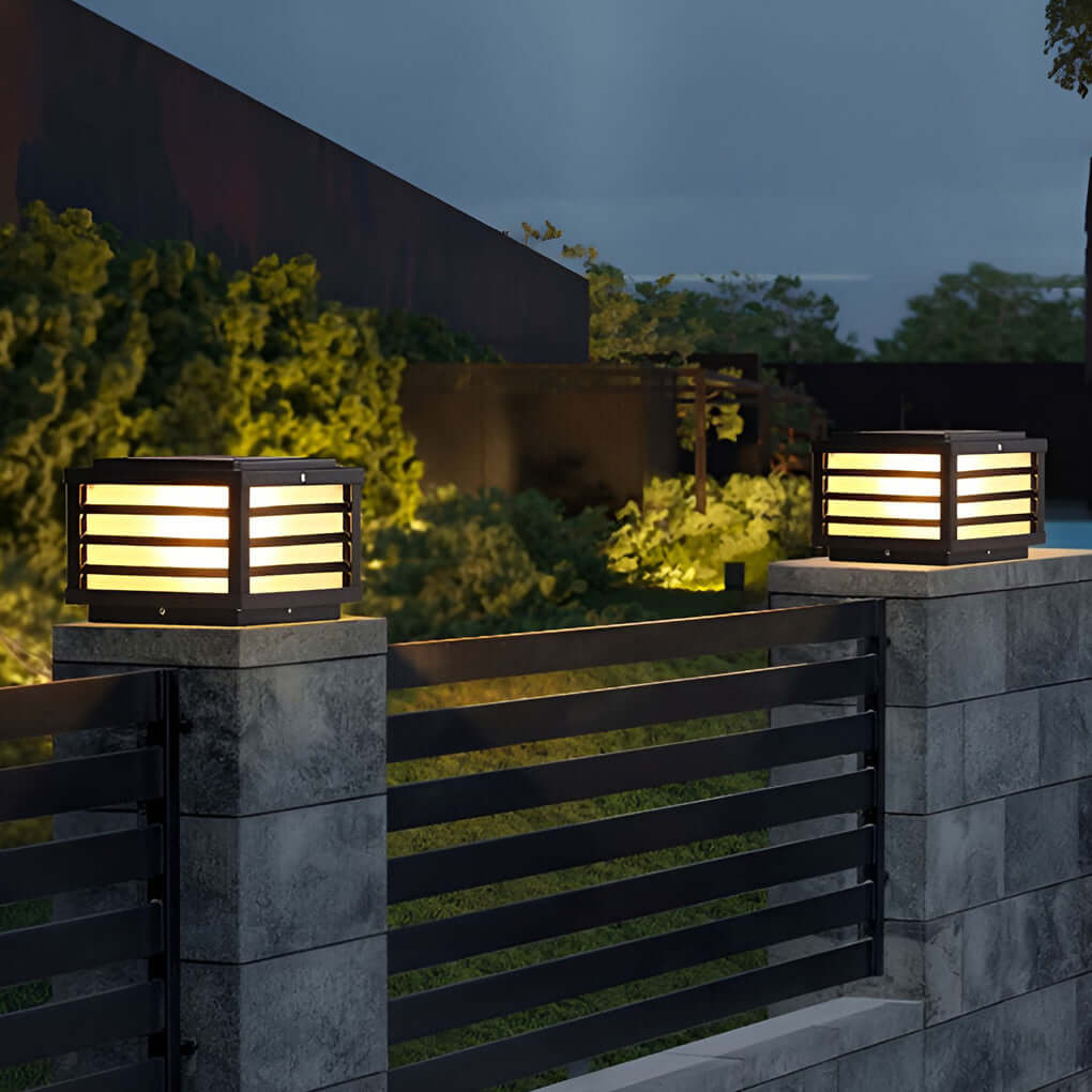 Black gate pillar light with a rectangular design, providing warm illumination near a garden pathway.