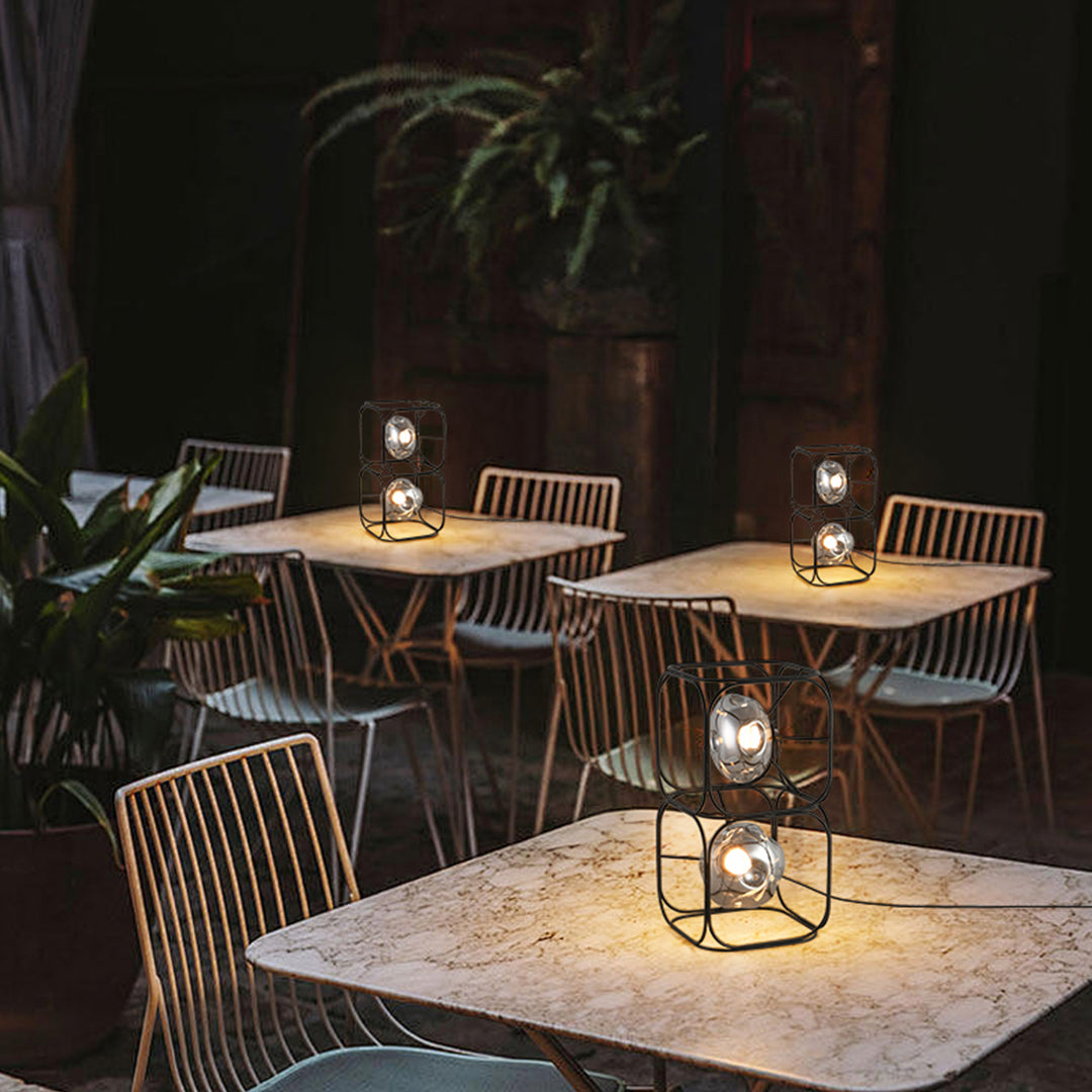 Black cube table lamp with geometric wire construction displayed against neutral commercial backdrop