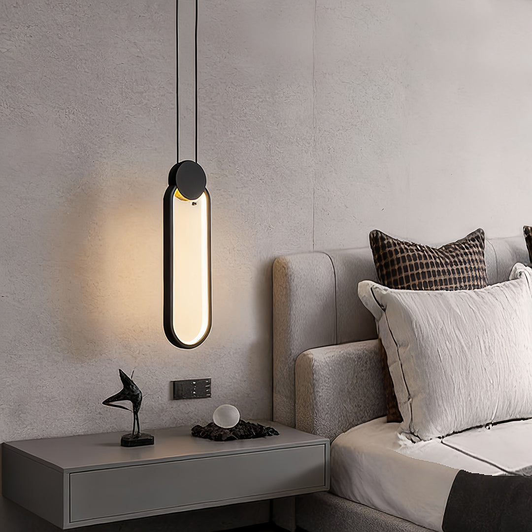 Vertical black geometric pendant light mounted next to upholstered bed headboard.