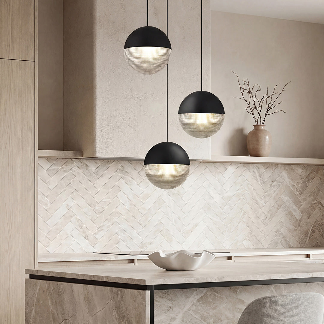 Trio of black globe pendant light fixtures over a marble kitchen island with wood cabinets.