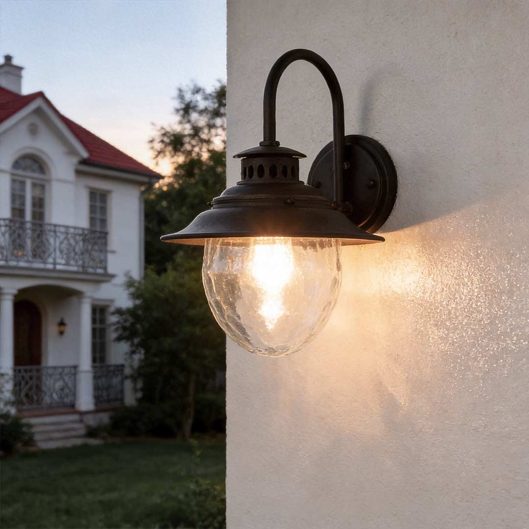 Black gooseneck wall light mounted on exterior wall, vintage outdoor fixture illuminating house facade with warm glow at dusk.