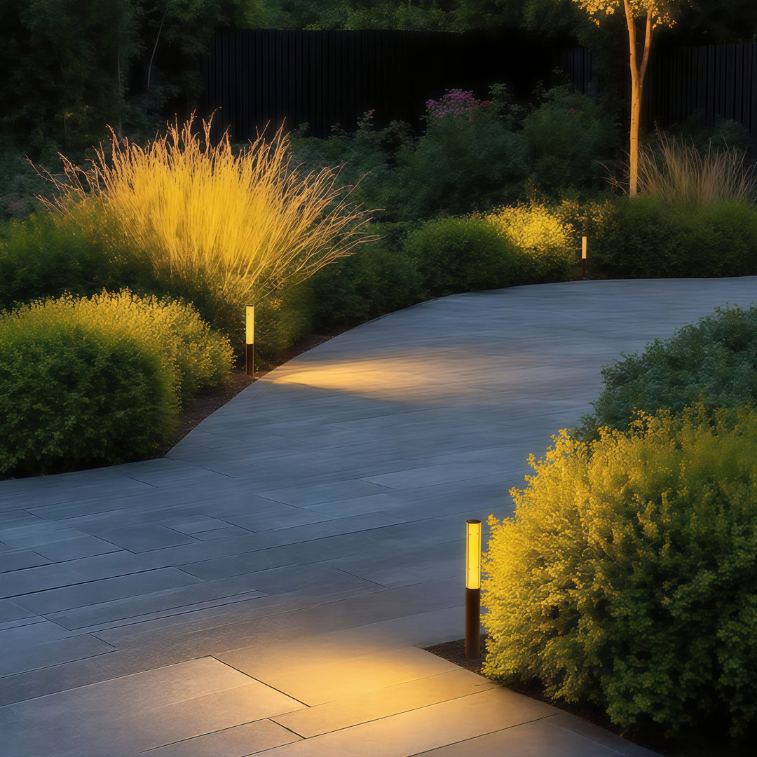 Black slim led bollard garden light installed beside pathway plants, offering warm vertical illumination.