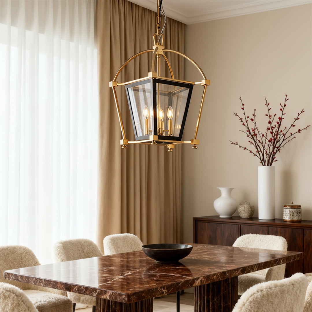 Gold lantern pendant light with black interior and three candle-style lights, hanging above a marble-top table in a warm, sophisticated dining setting.