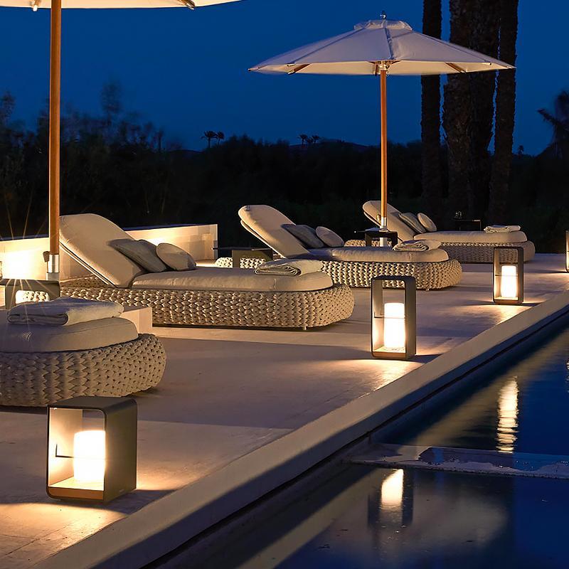 Black lantern outdoor light with open frame, creating cozy ambiance on patio with wicker chairs.