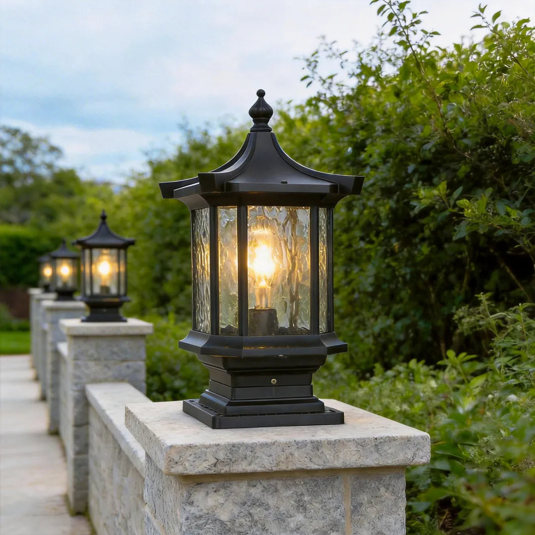 Black lantern pillar light placed on a stone wall post beside a landscaped pathway.