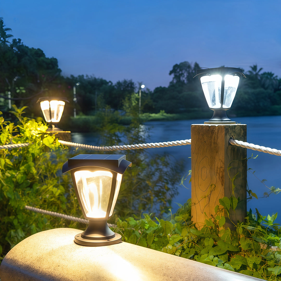 Black lantern solar light pillar lamps lighting up concrete posts along a lakeside rope railing at dusk.