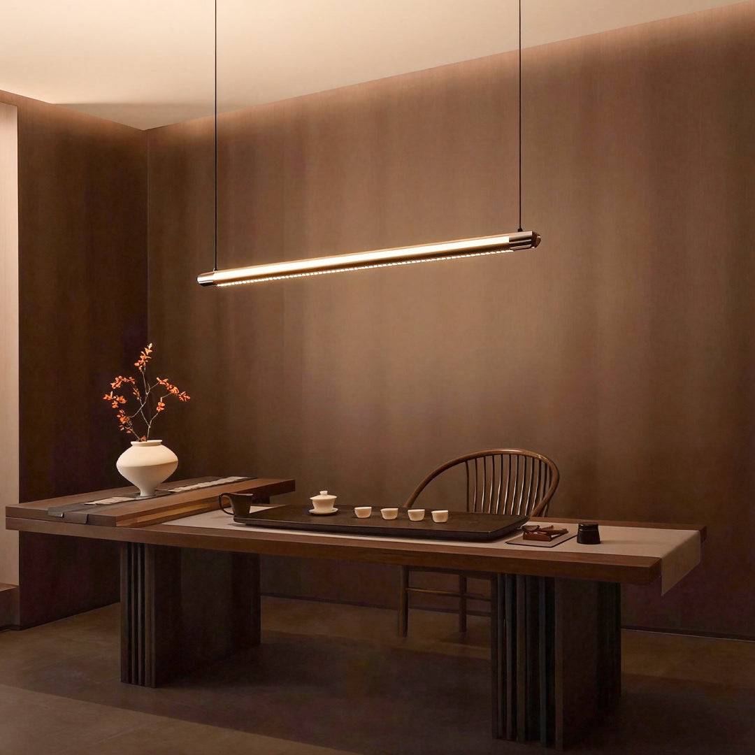 Black linear suspension light providing ambient illumination above wooden console table in warm-toned interior space