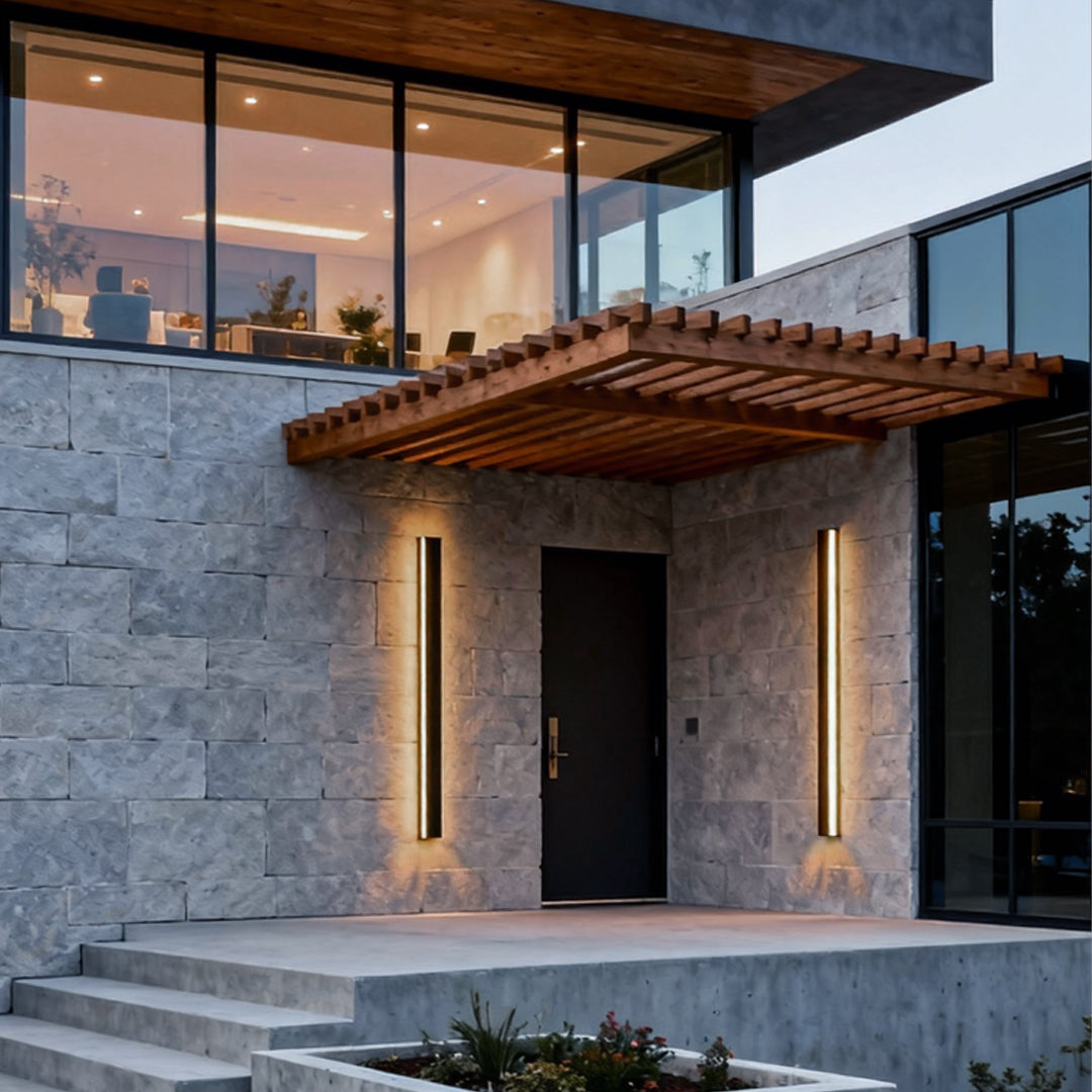 Black linear wall light illuminating a modern house entrance with sleek vertical glow.