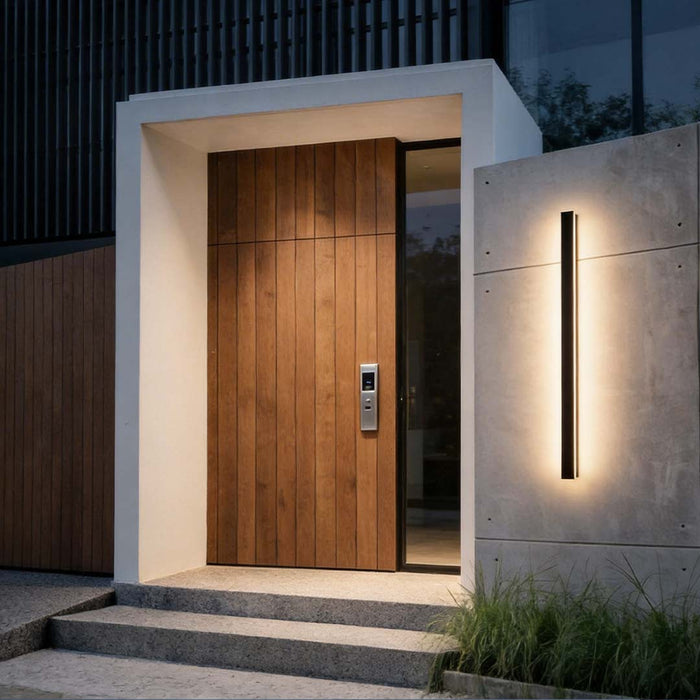 Black linear wall sconce illuminating a modern house entrance with sleek vertical light.