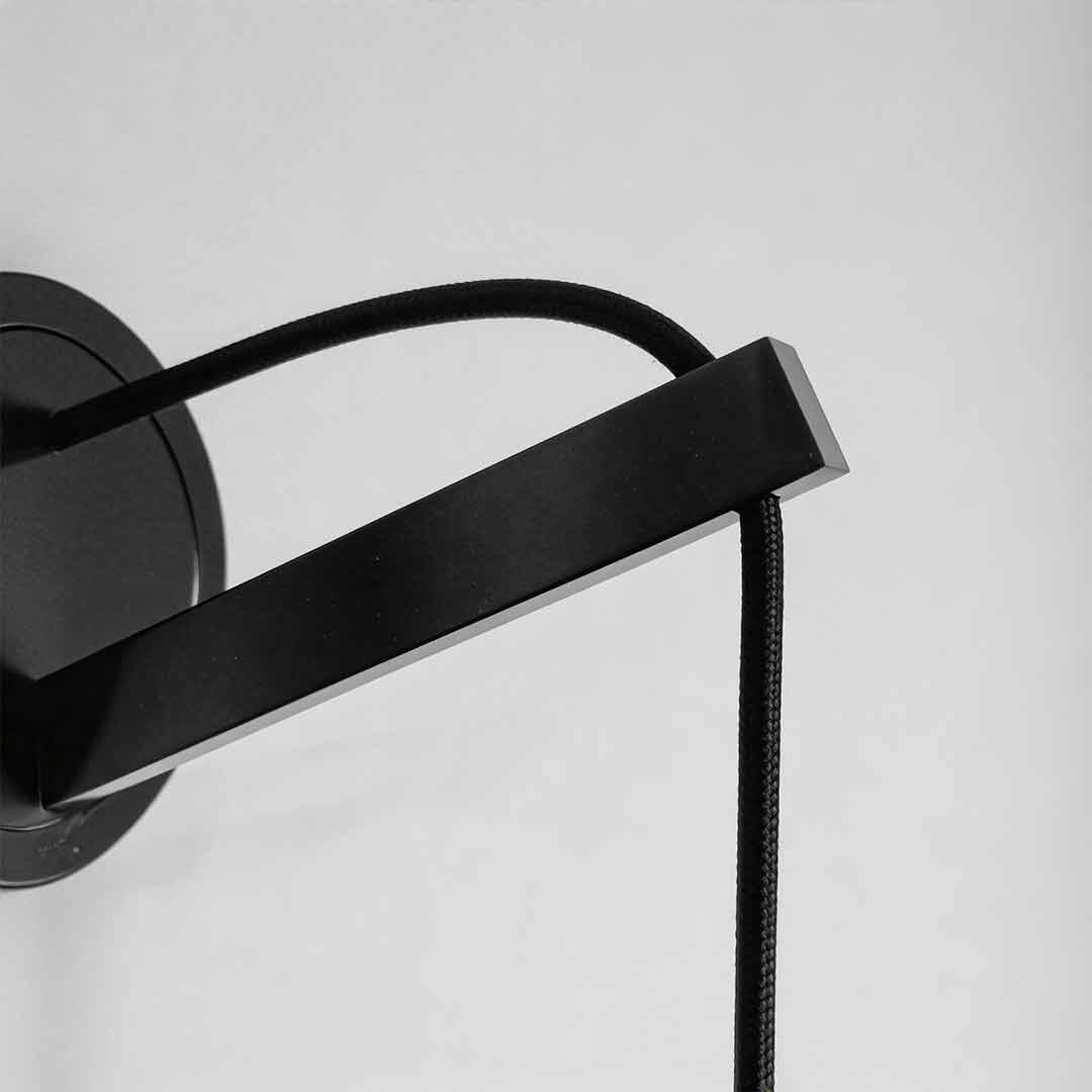 Close-up detail of the black metal bracket and cord of a bedside hanging wall lamp.
