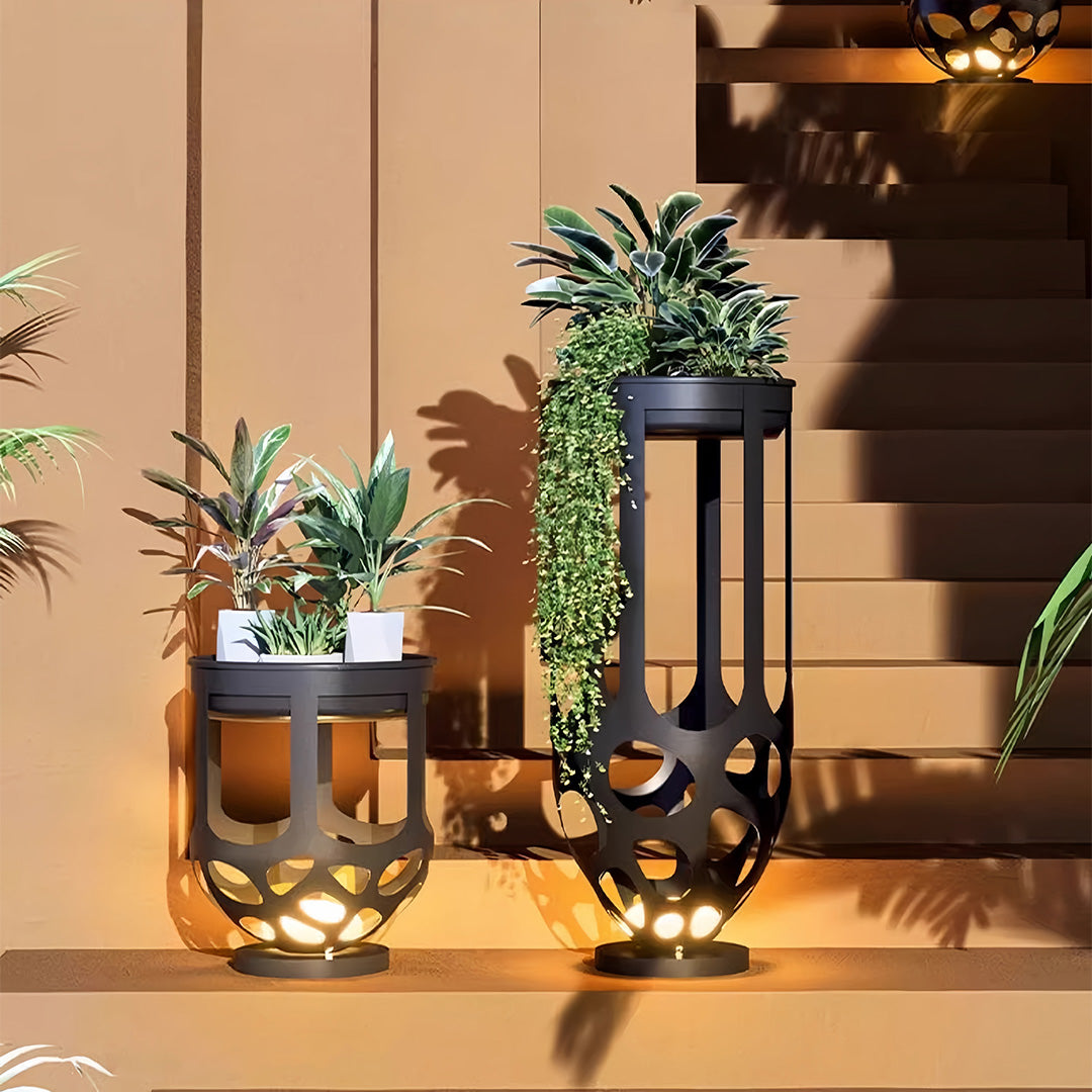 A pair of black metal lighted outdoor planter pots, one tall and one short, used as accent lighting on entryway stairs.