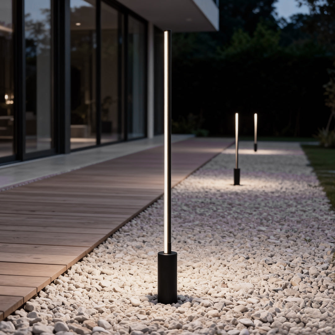 Minimalist black contemporary outdoor floor lamps illuminating a modern patio walkway at night.