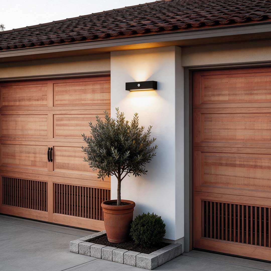 Black motion sensor outdoor wall light illuminating a modern garage entrance with warm security glow.