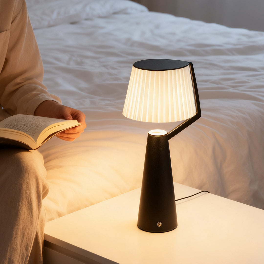 Black Nordic table lamp illuminating a book for reading beside a comfortable bed in a cozy evening setting.