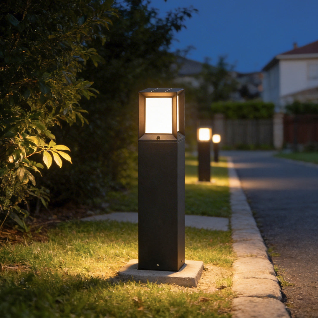 Row of black outdoor bollard lights illuminating a suburban neighborhood sidewalk path at dusk.