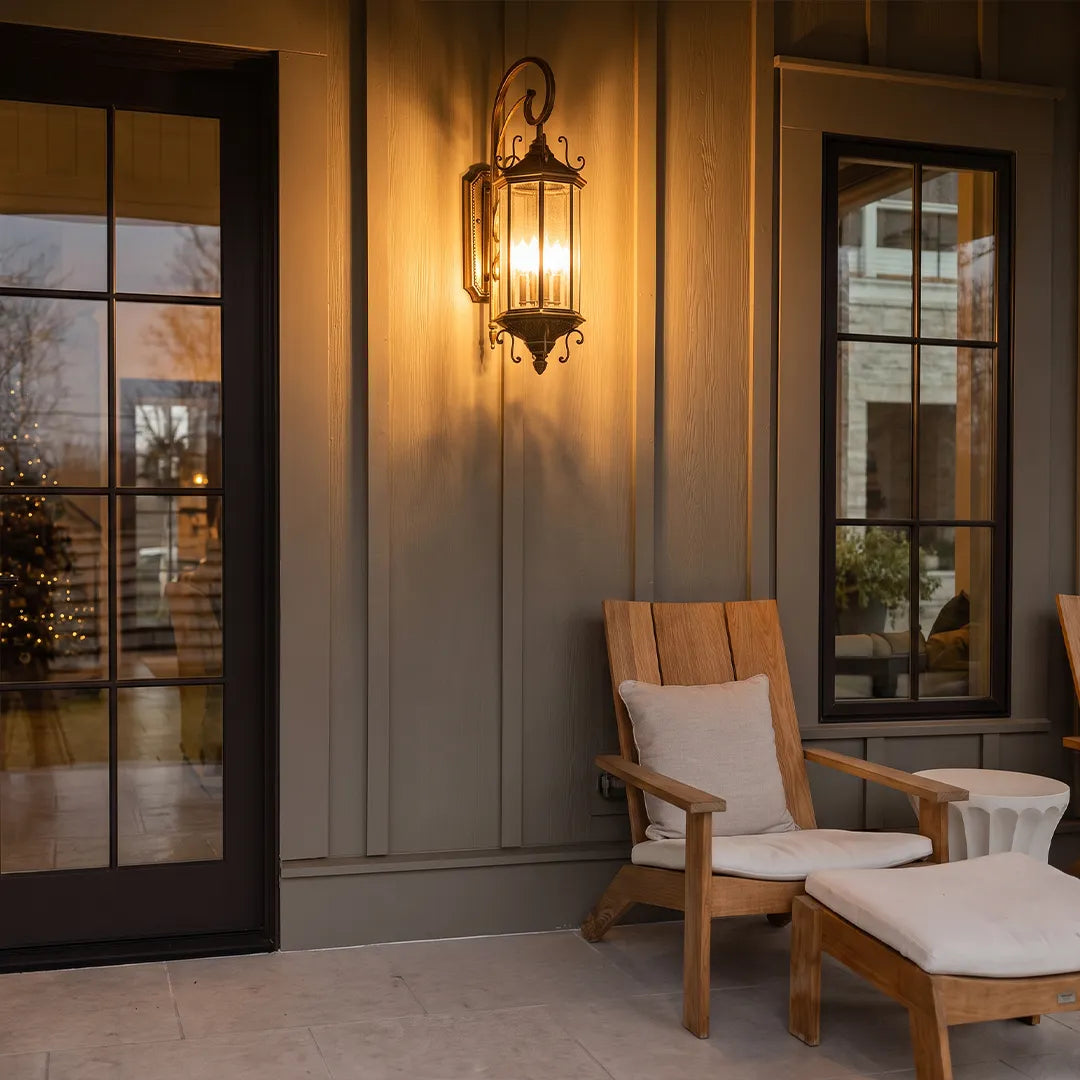 Black outdoor lantern sconce illuminating a covered porch seating area, complementing the dark exterior trim and window frames.