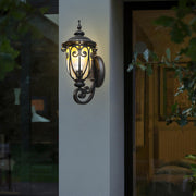Black outdoor lantern sconce beside a large window, casting a cozy glow during sunset.