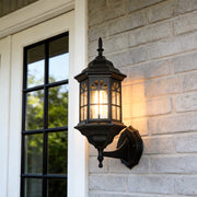 Black outdoor lantern sconce illuminating a modern house exterior with warm, inviting glow.